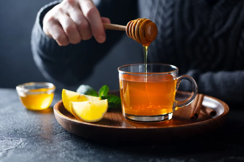 cup of tea with pouring honey and lemon grey background