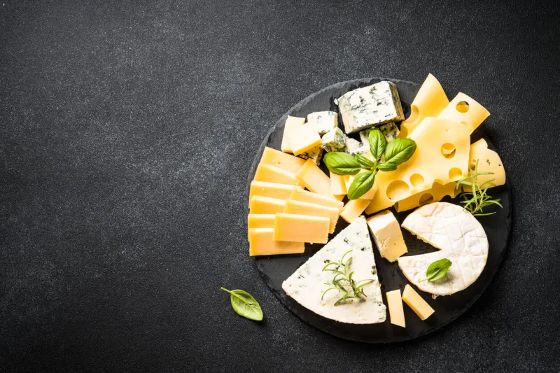 cheese platter with craft cheese assortment on slate board at black background top view with copy space