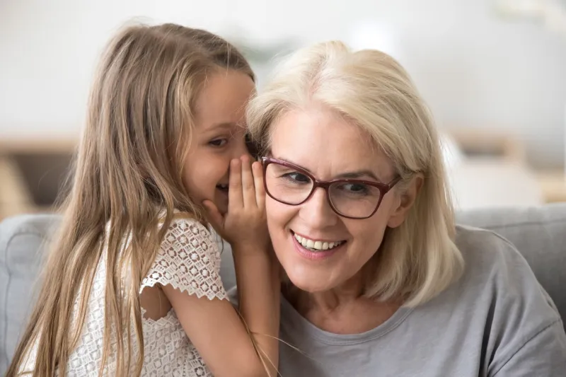 cute little granddaughter whispering in ear telling secret to understanding smiling grandma, kid girl secretly talking to granny having fun gossiping, trust in grandmother and grandchild relations