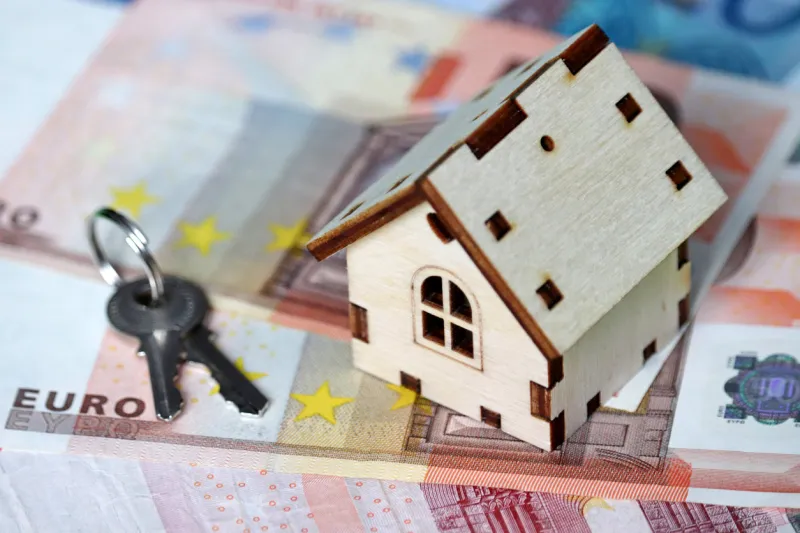 wooden house model and keys on background of euro banknotes