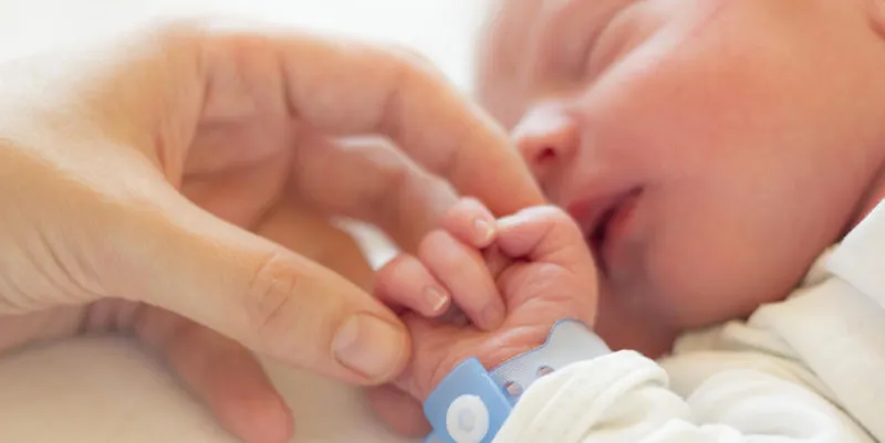 newborn baby boy sleeping in his crib, his mother's hand holding his little hand