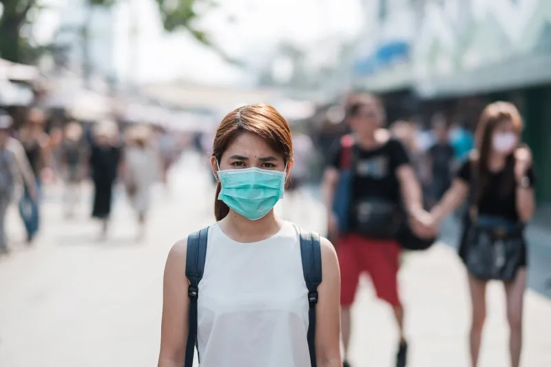 young asian woman wearing protection mask against novel coronavirus (2019-ncov) or wuhan coronavirus at chatuchak weekend market, landmark and popular for tourists attractions in bangkok, thailand