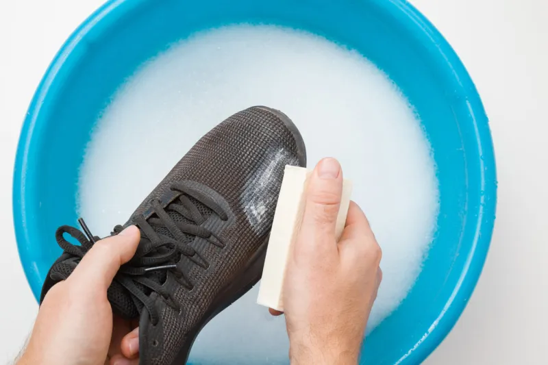 man hands washing black sport shoe with natural laundry soap above blue basin regular care about sneakers point of view shot closeup top view