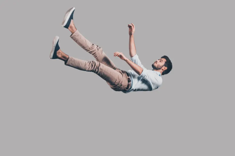 mid-air shot of handsome young man falling against grey background