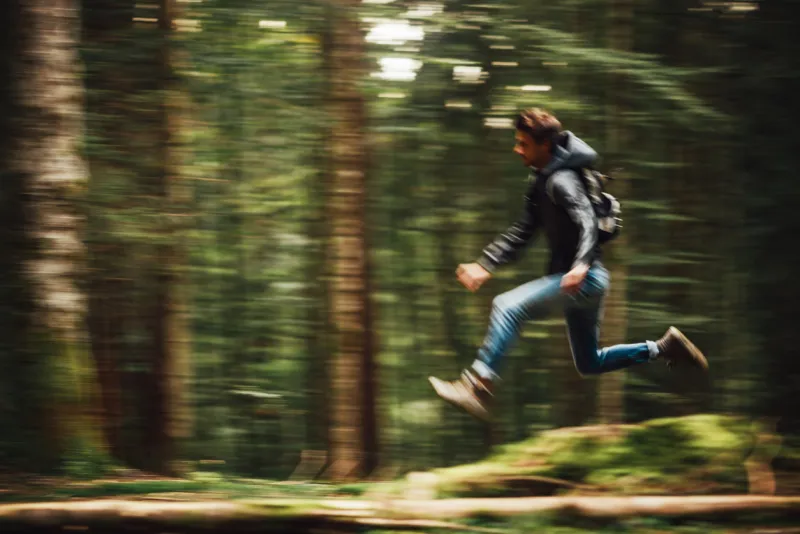 hooded young man with backpack running in the forest