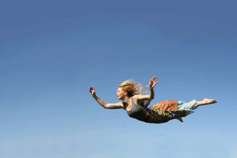 a young woman is falling as if flying through the air in front of a blue sky background