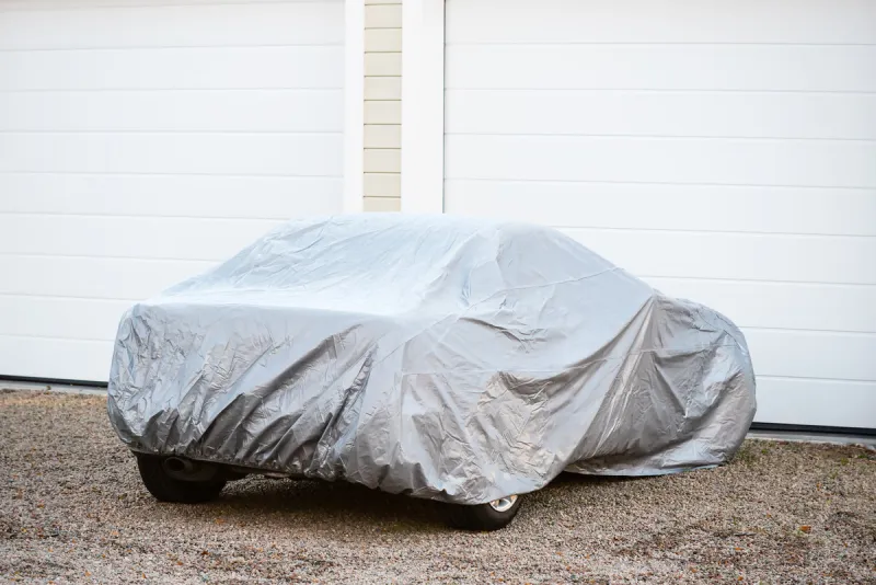 sports car under silver colored cover outside a closed garage