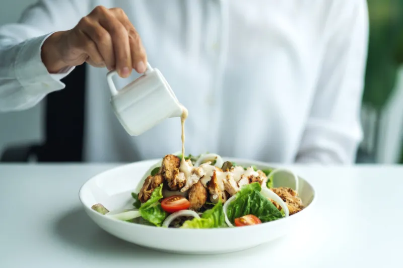 closeup image of a woman pouring dressing into a chicken salad
