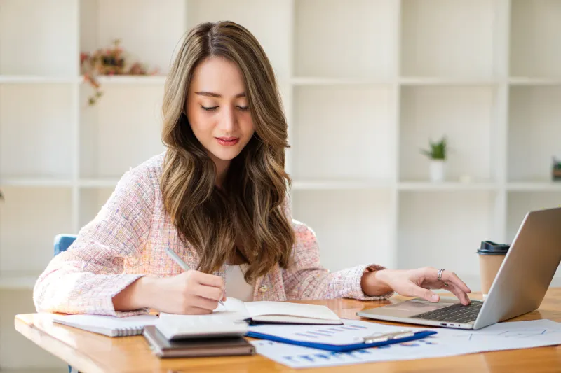 smiling beautiful asian businesswoman analyzing charts and graphs showing market changes using laptop at company desk reading financial charts