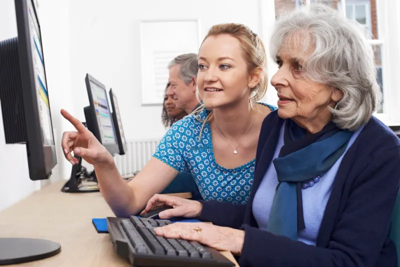 tutor helping senior woman in computer class