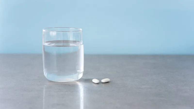 white medical pills and a glass of water on a light blue background, copy the space the concept of medicine and pharmacy