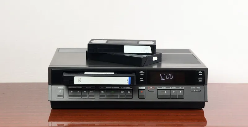an old vintage videotape recorder from the 1980s stands on a dark table with a videotape retro vcr
