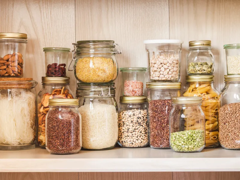 shelf in the kitchen with various cereals and seeds - peas split, sunflower and pumpkin seeds, beans, rice, pasta, oatmeal, couscous, lentils, bulgur in glass jars