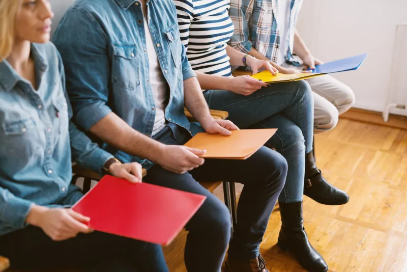 close up view of young people sitting in chairs with folders before the job interview in the waiting room