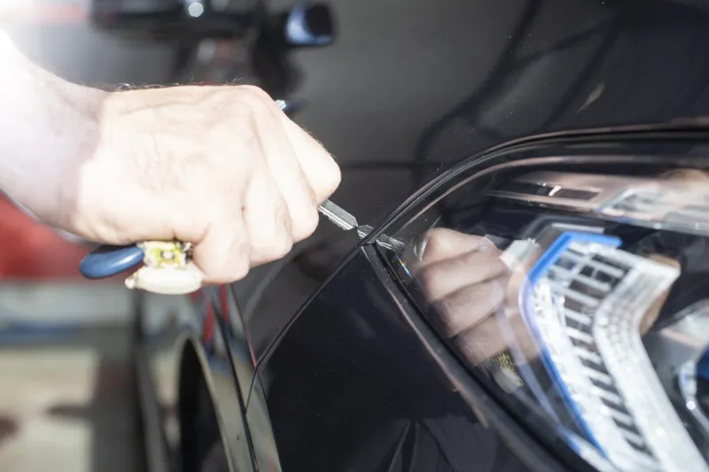 hand holding a key and starting to scratch a luxury car, headlights close up