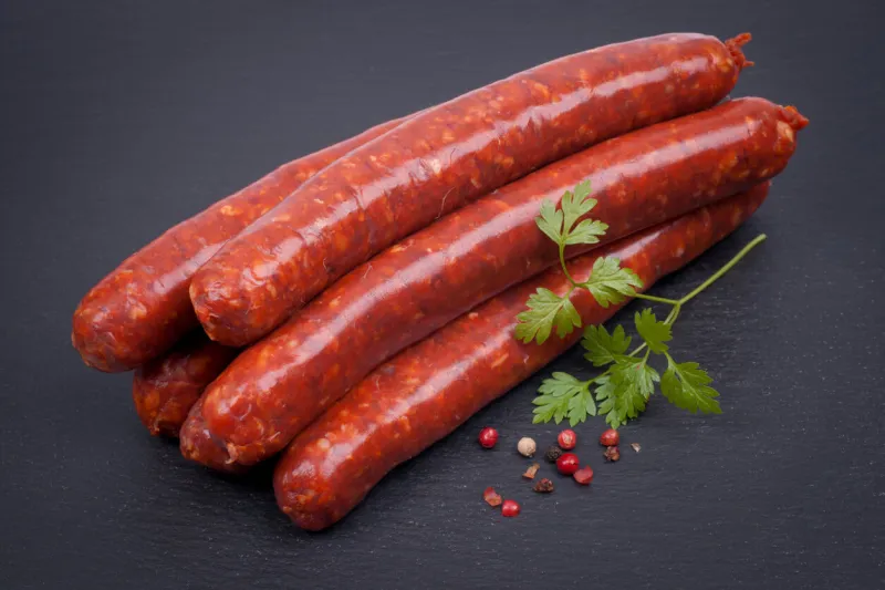 lamb sausage pieces stacked on a black surface with garnish