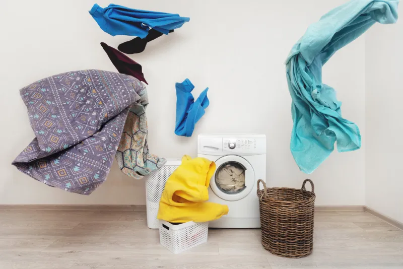 concept of funky and easy laundry process white washing machine standing inside flat with bright interior near flying multicolored clothes