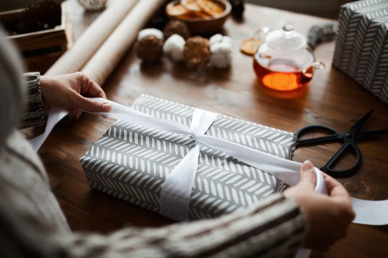 close-up of woman sitting at the table and decorating gift box with ribbon for christmas