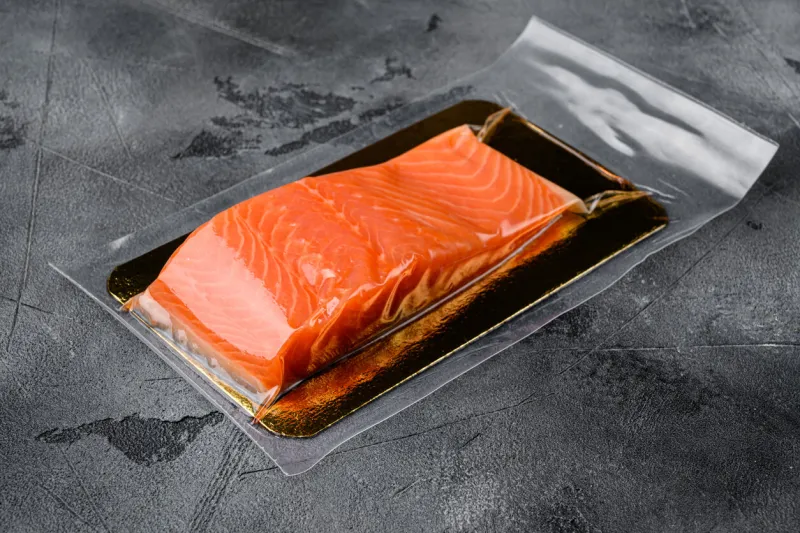 red fish fillet in vacuum pack set, on gray stone table background, with copy space for text