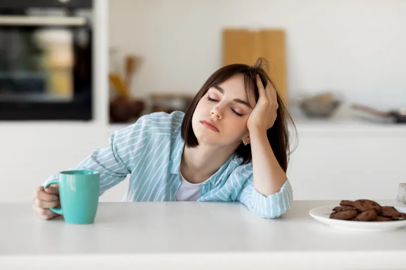 sleepy young woman drinking coffee, feeling tired, suffering from insomnia and sleeping disorder sad female sitting in modern kitchen interior, empty space