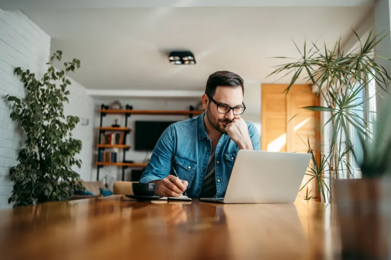 serious man looking at laptop and taking notes in notebook, portrait
