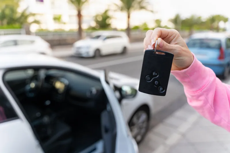 hand of woman holding card key by white vehicle with open door car rental, free ride, insurance concepts