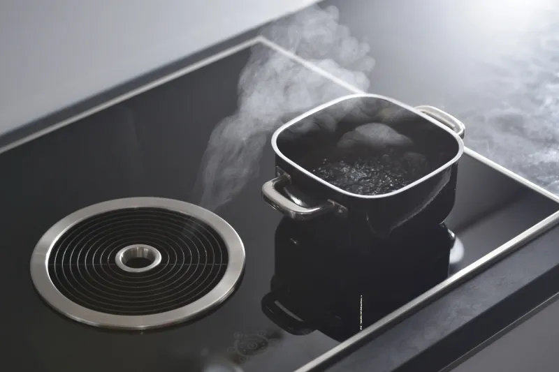 modern electric induction cooker with built-in ventilation and extractor hood which draws steam from boiling water in a pan steam from a boiling pot is drawn into the integrated range hood