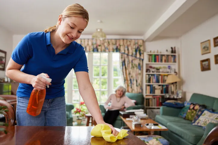 female home help cleaning house and talking to senior woman