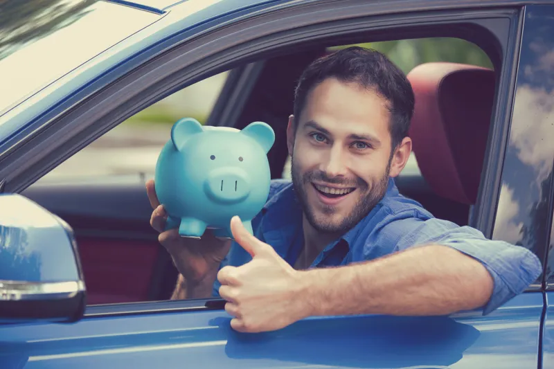 happy man sitting inside his new car holding piggy bank showing thumbs up