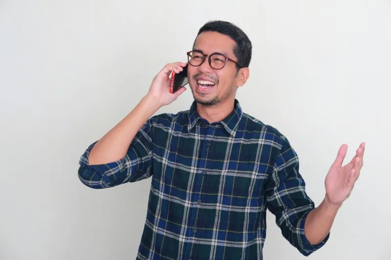 adult asian man laughing happy when answering a mobile phone call