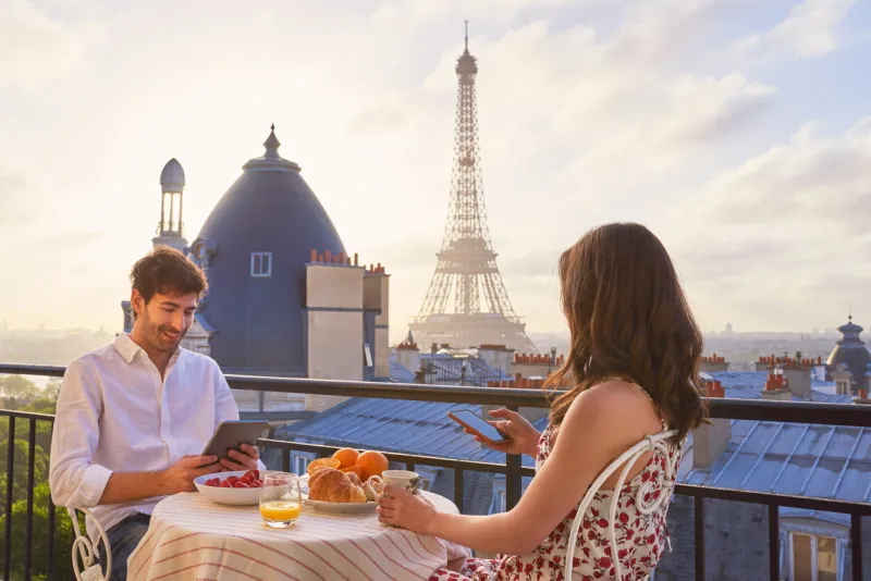 shot of a young couple having breakfast on the balcony of an apartment overlooking the eiffel tower in paris, france