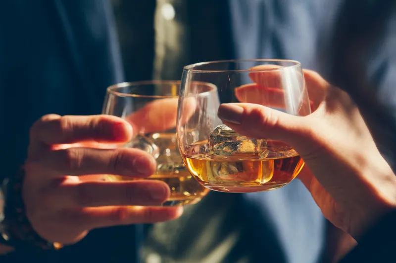 man and woman celebrating with whiskey glasses