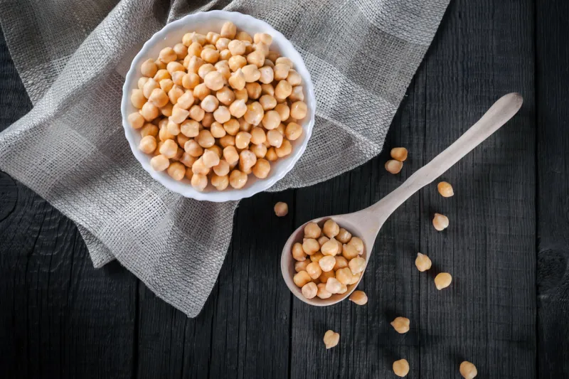 steamed gold chickpeas in bowl on tablecloth with wooden spoon, tasty vegan food, top view