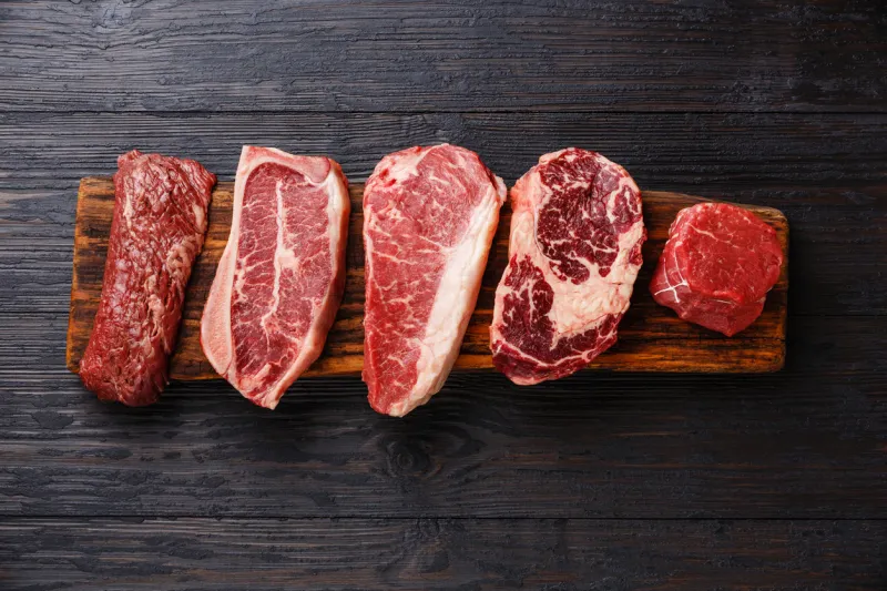 variety of raw black angus prime meat steaks machete, blade on bone, striploin, rib eye, tenderloin fillet mignon on wooden board copy space