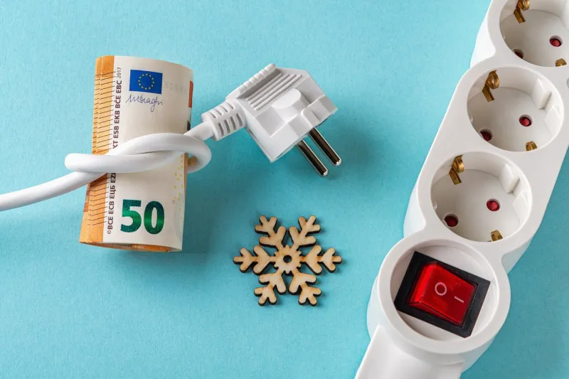 white electric plug tied to a knot on a fifty euro banknotes, snowflake and power strip over blue background rise in electricity prices in the cold season increasing of electricity cost concept