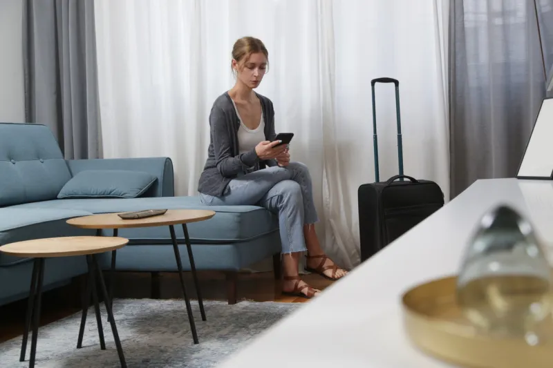 young woman traveller with smartphone and luggage in hotel room