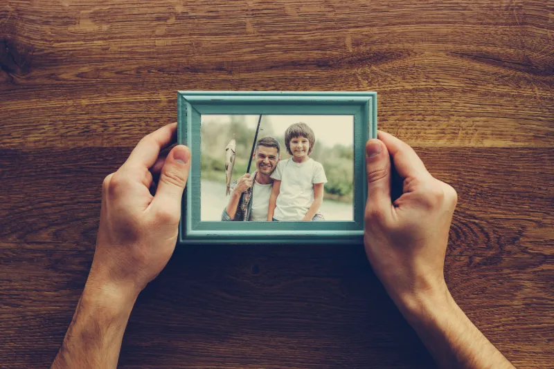 close-up top view of man holding photograph of himself and his son fishing over wooden desk