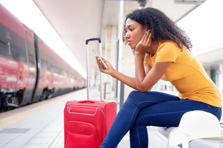 afro woman waiting for the train in station platform using cell phone