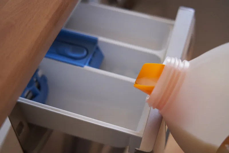closeup pouring detergent into the compartment of a washing machine