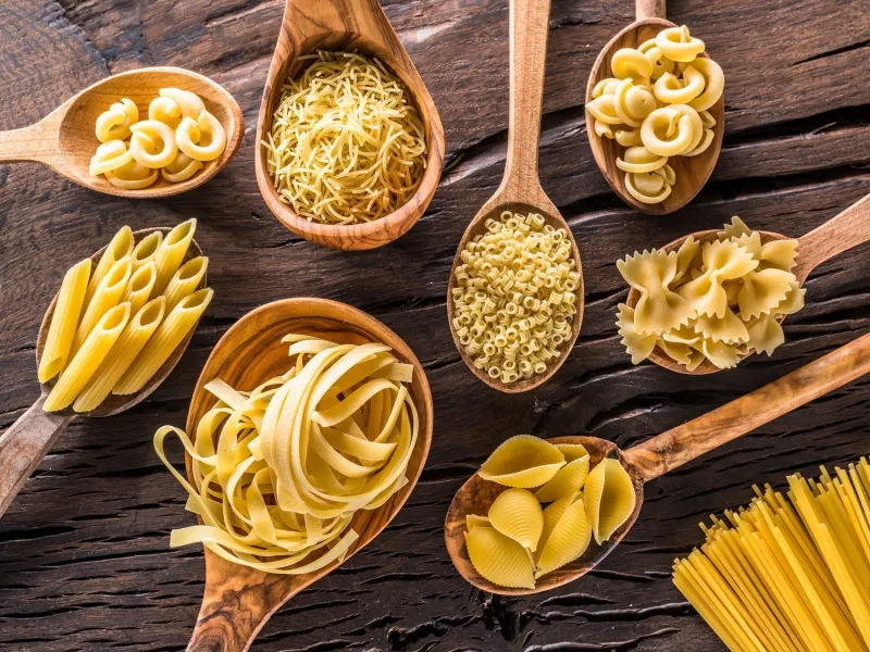 different pasta types in wooden spoons on the table top view