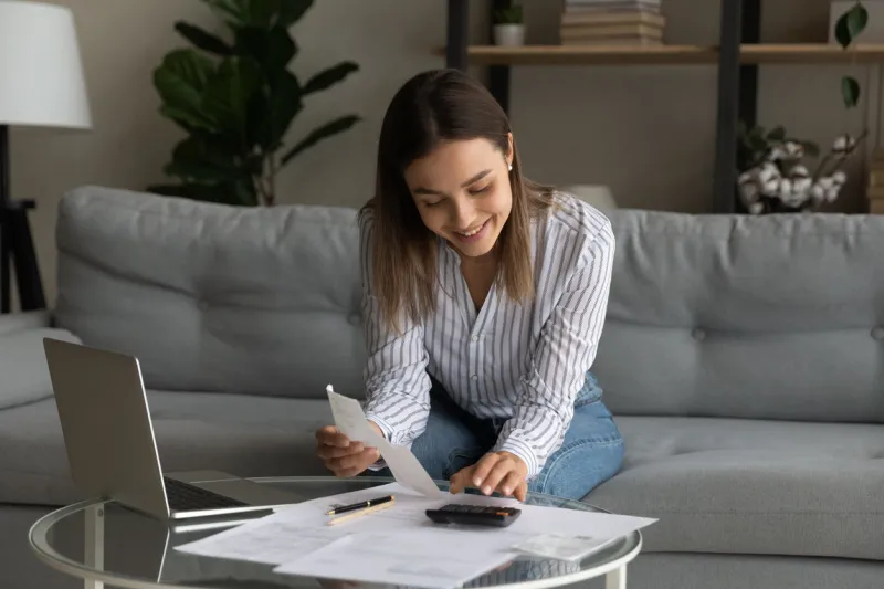 happy young woman holding paper bills in hands, calculating expenditures, paying bills or services online in computer application, feeling satisfied with enough money, investment payments concept