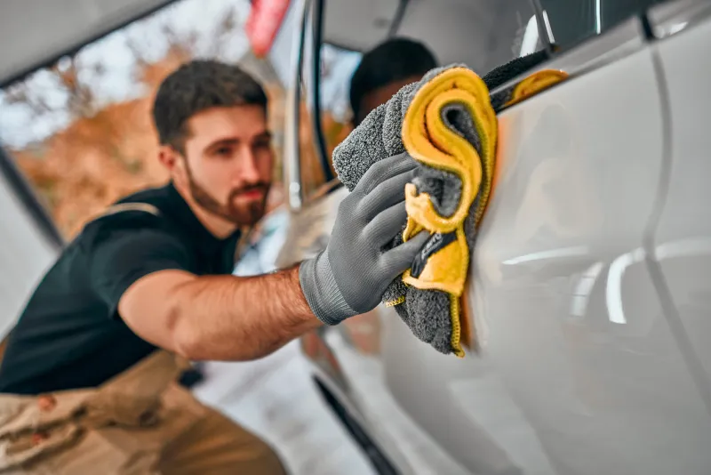 man after washing wipes white car with a rag at car wash selective focus