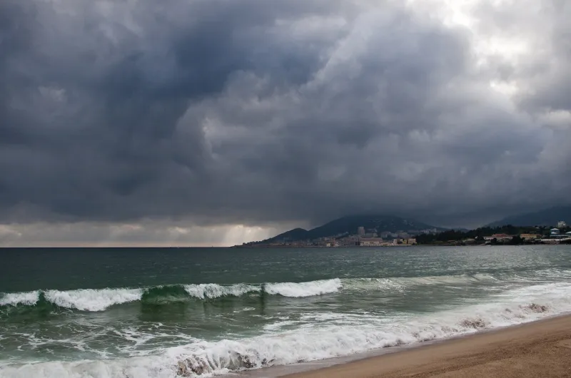 the town of ajaccio in corsica in the background with a beach in the foreground and the sea under a stormy sky