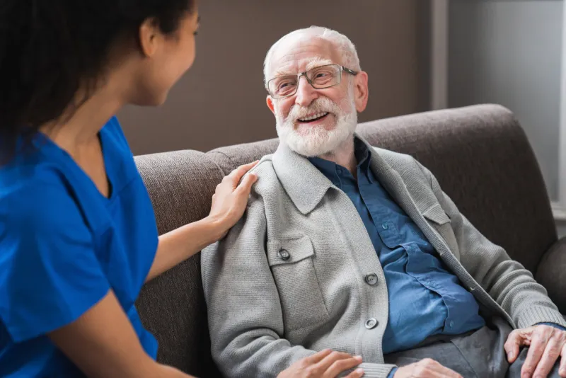 young friendly african female caregiver talking chatting to happy senior man in hallway of nursing home picture of smiling nurse assisting senior elderly man