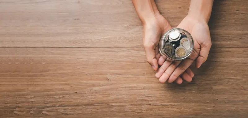 woman hand holding money coin in glass jar on wooden background, donation, saving, fundraising charity, family finance plan concept, superannuation, financial crisis concept, top view