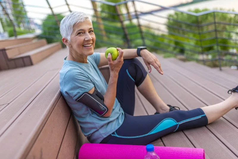 sporty woman eating apple beautiful woman with gray hair in the early sixties relaxing after sport training healthy age mature athletic woman eating an apple after sports training