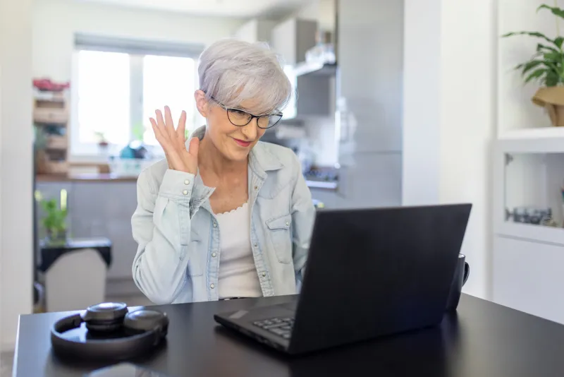 senior woman using computer at home for a video call - smiling lady waving at people on a call - new normal lifestyle in digital age