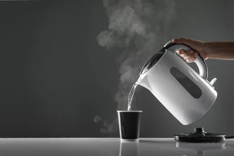 electric white kettle pouring water in cup on table on grey background