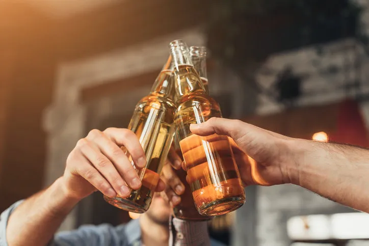 men clinking bottles of beer together, sitting in bar, closeup