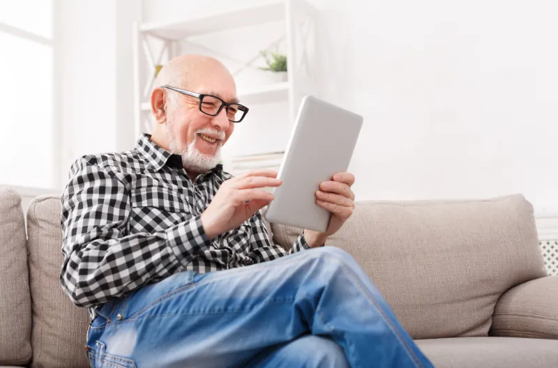 smiling senior man reading news on digital tablet cheerful excited mature male using portable computer at home, copy space